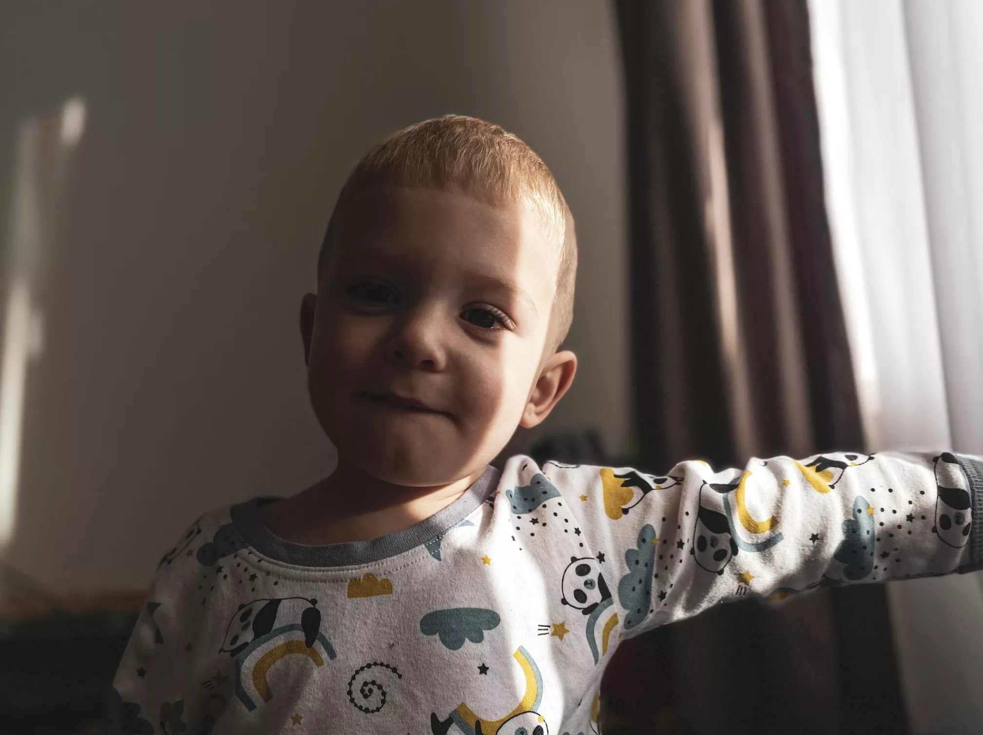 Хлопчик стоїть в кімнаті і на нього світить сонце з вікна